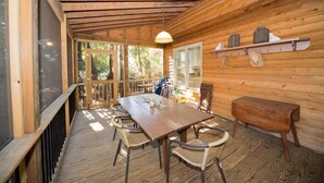 A wooden cabin with a dining table, chairs, a small bench, and a hanging light fixture.