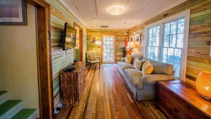 A cozy room with wooden floors, a sofa, a chair, a TV, and a lamp.