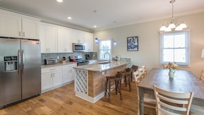 Una cocina moderna con armarios blancos, electrodomésticos de acero inoxidable y una isla de madera con taburetes de bar.