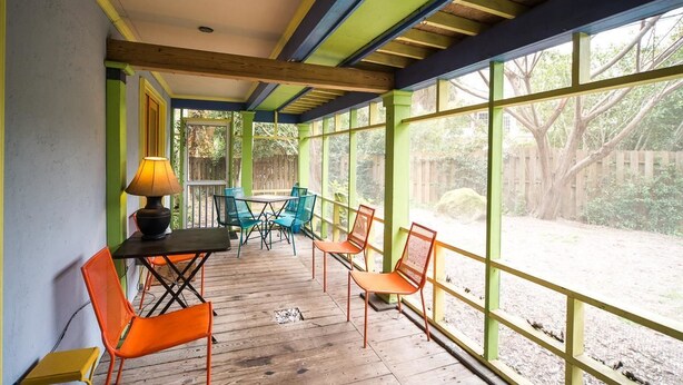 Un patio coperto con pavimento in legno, pareti dipinte di verde e giallo, e ampie finestre che offrono vista sul paesaggio.