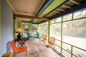 Un patio cubierto con suelo de madera, paredes pintadas de verde y amarillo, y amplias ventanas con vistas al exterior.