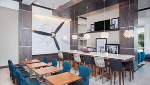 Un espace de salle à manger moderne avec une longue table, des chaises bleues et des luminaires suspendus.