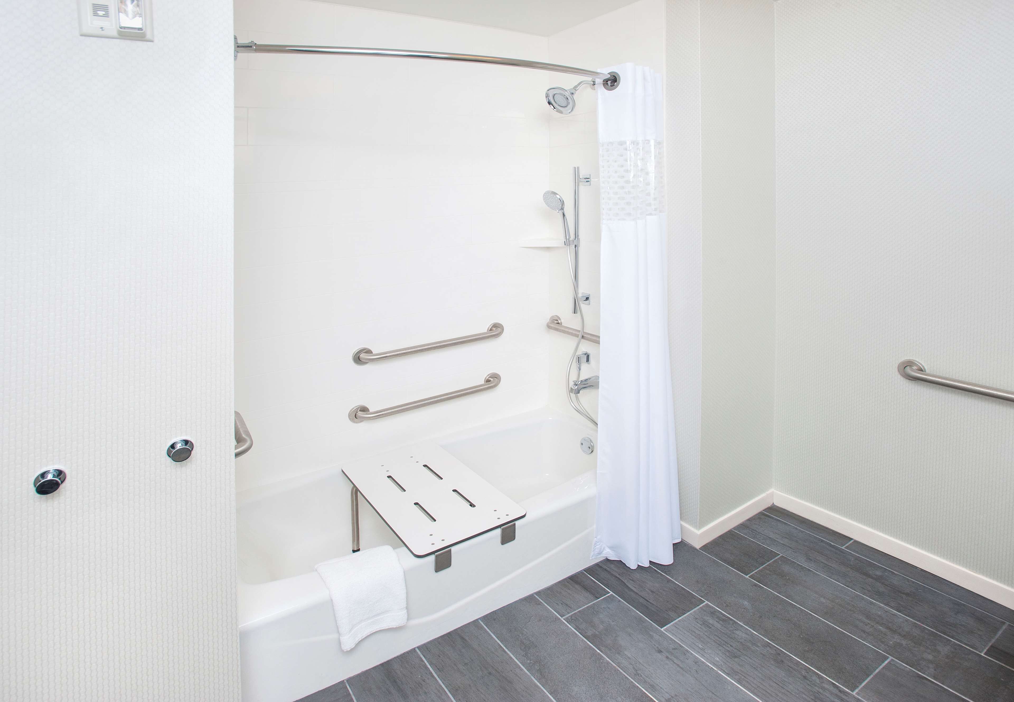 Ein modernes Badezimmer mit barrierefreier Dusche, Haltegriffen, einer weißen Badewanne und einem Handtuchhalter.