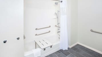 Ein modernes Badezimmer mit barrierefreier Dusche, Haltegriffen, einer weißen Badewanne und einem Handtuchhalter.