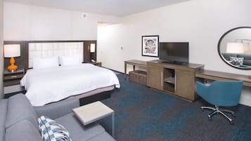 A hotel room with a bed, a desk, a chair, a sofa, a TV, and a mirror.