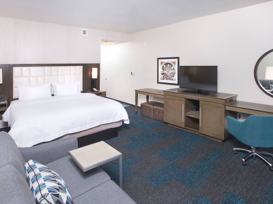A hotel room with a bed, a desk, a chair, a sofa, a TV, and a mirror.