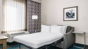 Une chambre d’hôtel avec un lit, un bureau, une chaise, une lampe fixée au mur et un tableau encadré accroché au mur.