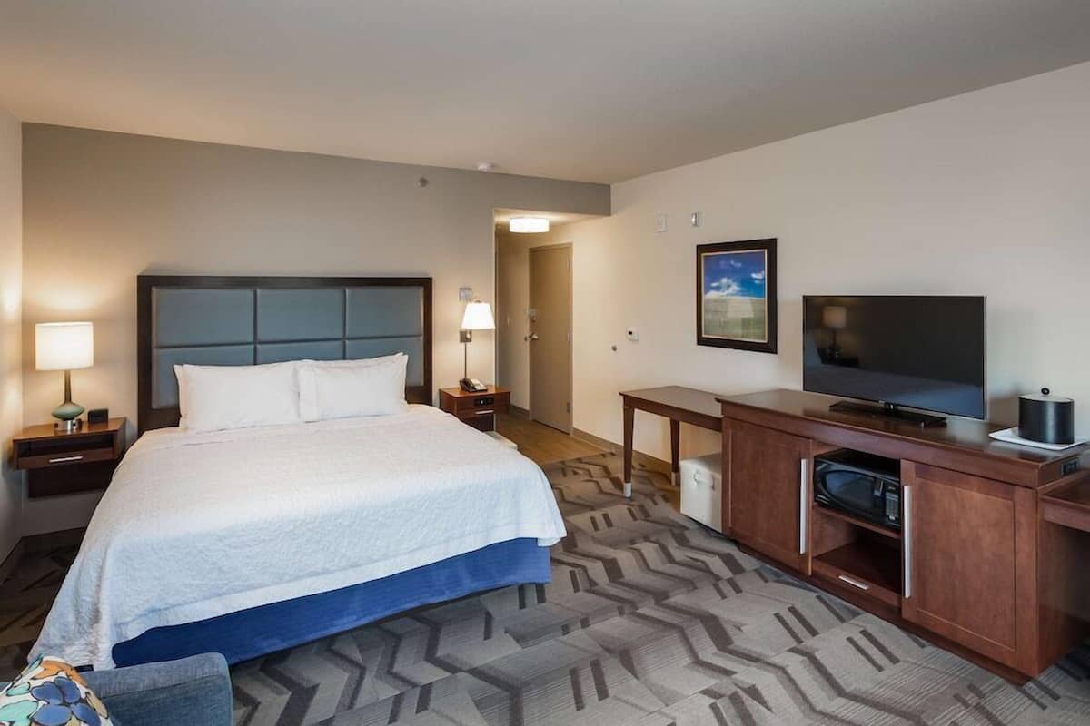 A hotel room with a large bed, a TV, a desk with a computer, and a lamp.