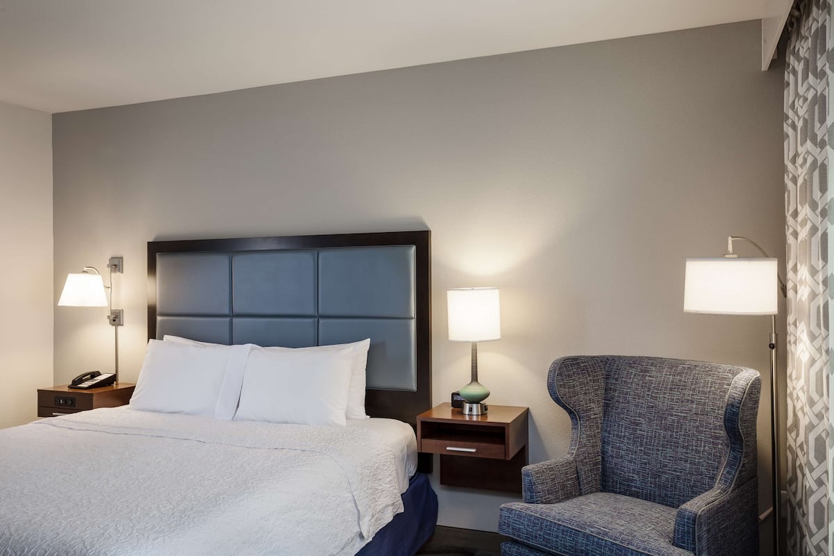 A hotel room with a bed, two bedside tables, a chair, and two lamps.