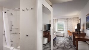 A modern hotel room with a shower, a desk, a television, and a view of the outdoors.
