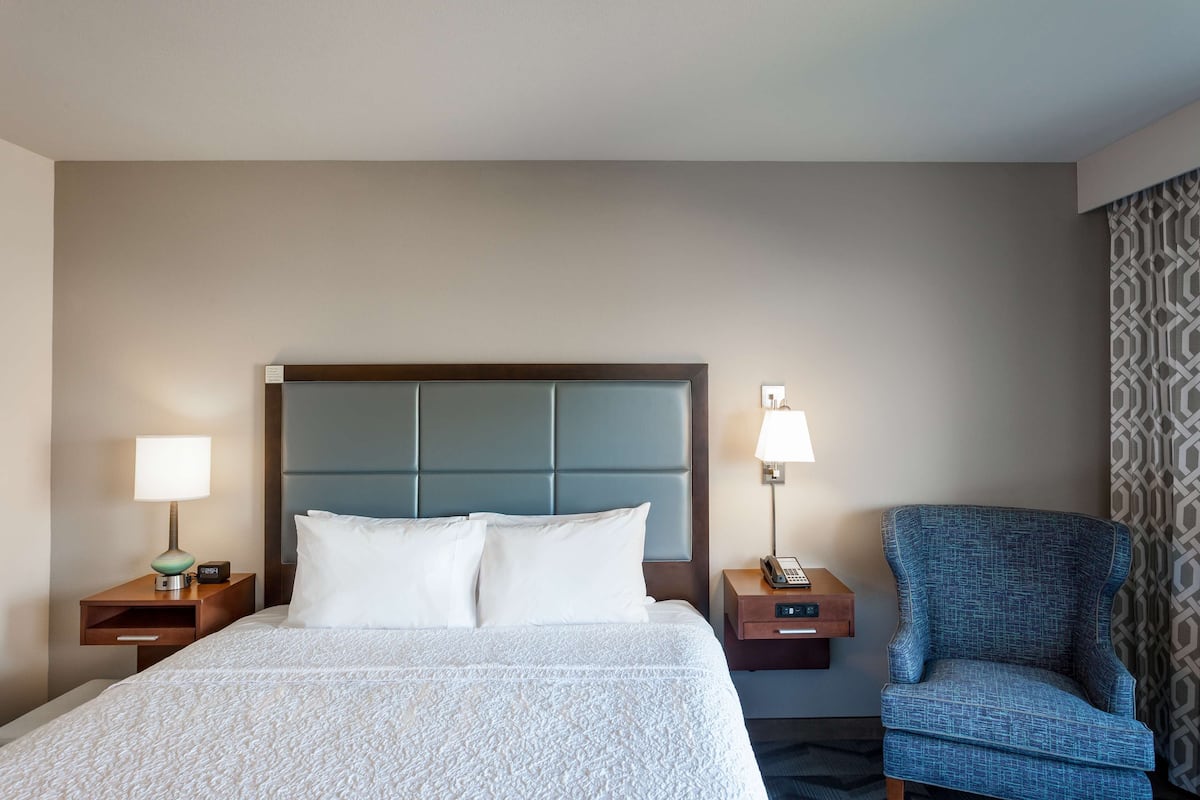 A hotel room with a bed, two bedside tables, a chair, and a headboard.