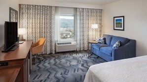 A hotel room with a desk, chair, sofa, and bed.
