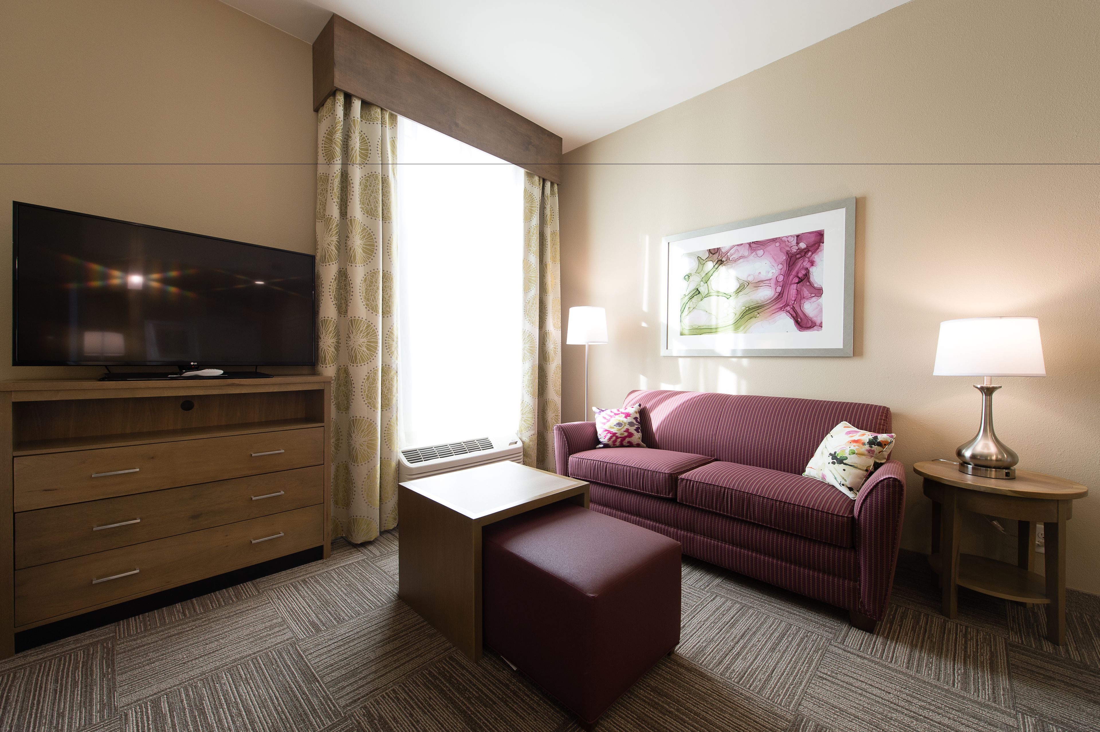 A hotel room with a flat-screen TV, a sofa, a small table, a lamp, and a painting on the wall.