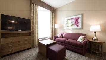 A hotel room with a flat-screen TV, a sofa, a small table, a lamp, and a painting on the wall.