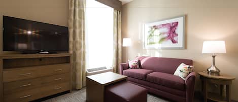 Une chambre d’hôtel équipée d’une télévision à écran plat, d’un canapé, d’une petite table, d’une lampe et d’un tableau au mur.