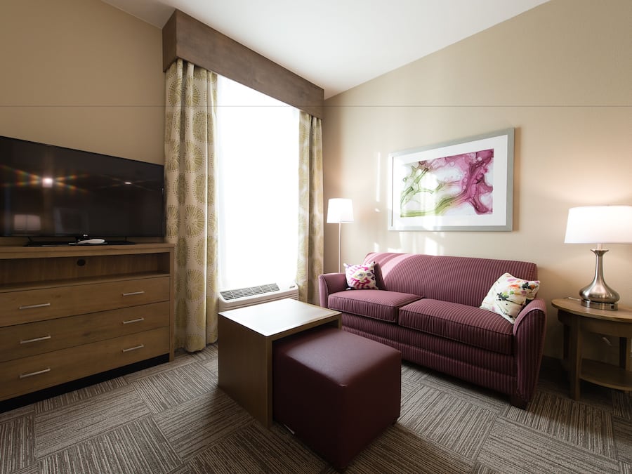 A hotel room with a flat-screen TV, a sofa, a small table, a lamp, and a painting on the wall.