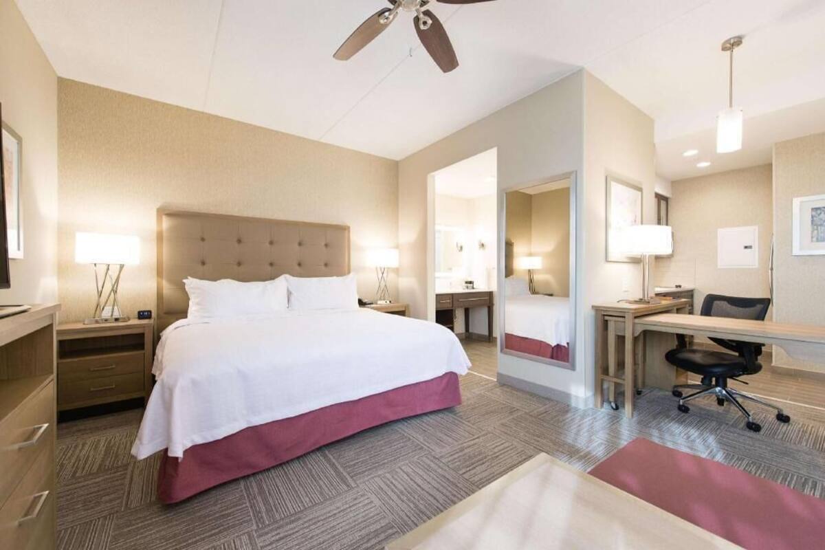 Una habitación de hotel con cama, escritorio, silla y ventilador de techo.