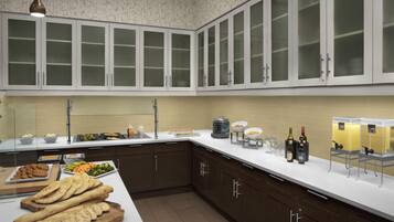 A modern kitchen with dark brown cabinets, a white countertop, and a variety of food items displayed.