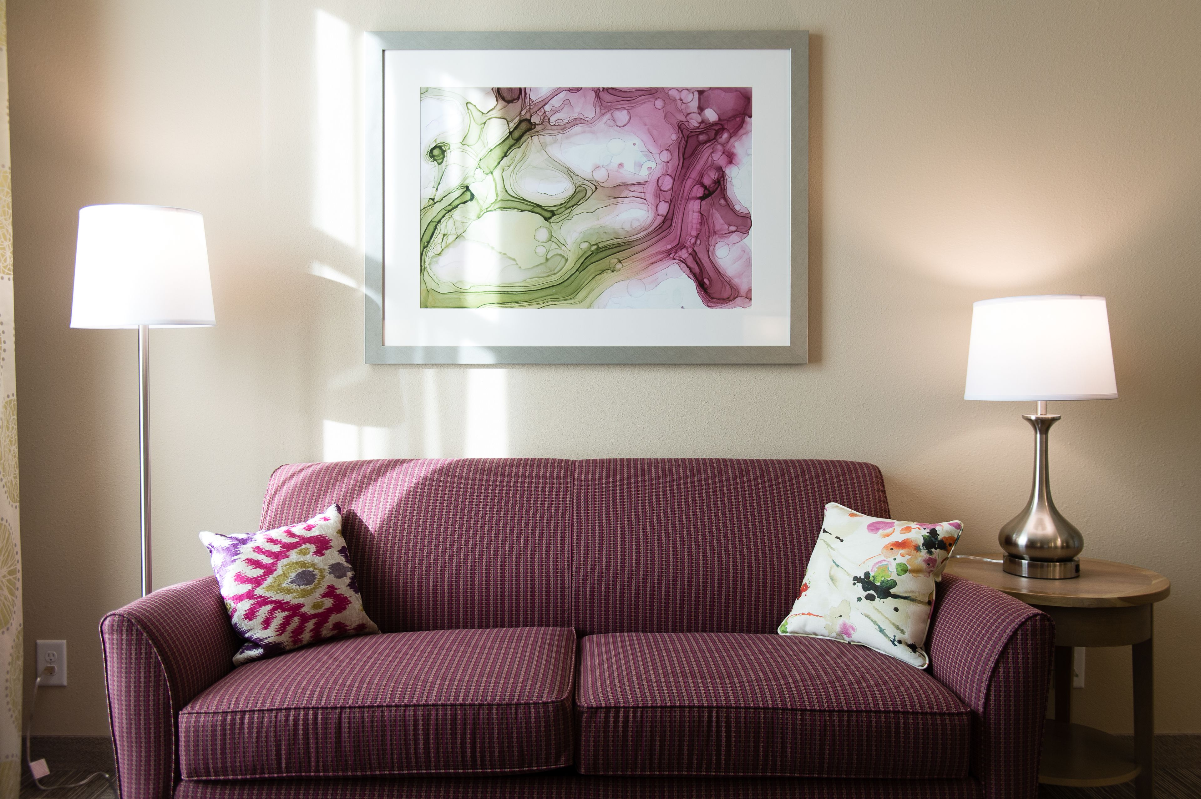 A room with a purple sofa, two lamps, and a framed abstract painting on the wall.
