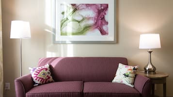 A room with a purple sofa, two lamps, and a framed abstract painting on the wall.