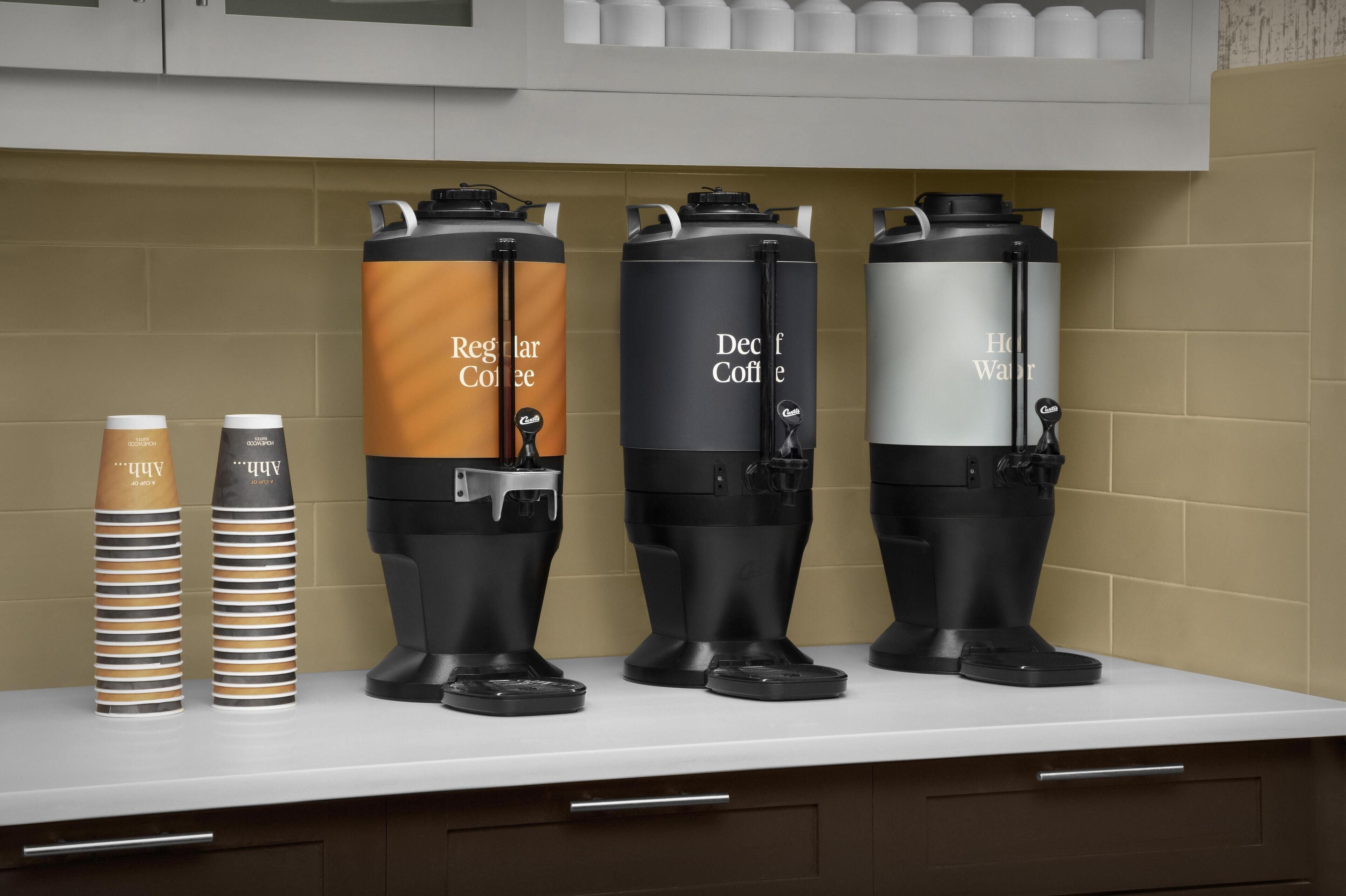 Eine Küchenarbeitsplatte mit drei Kaffeemaschinen und zwei Stapeln Kaffeetassen.