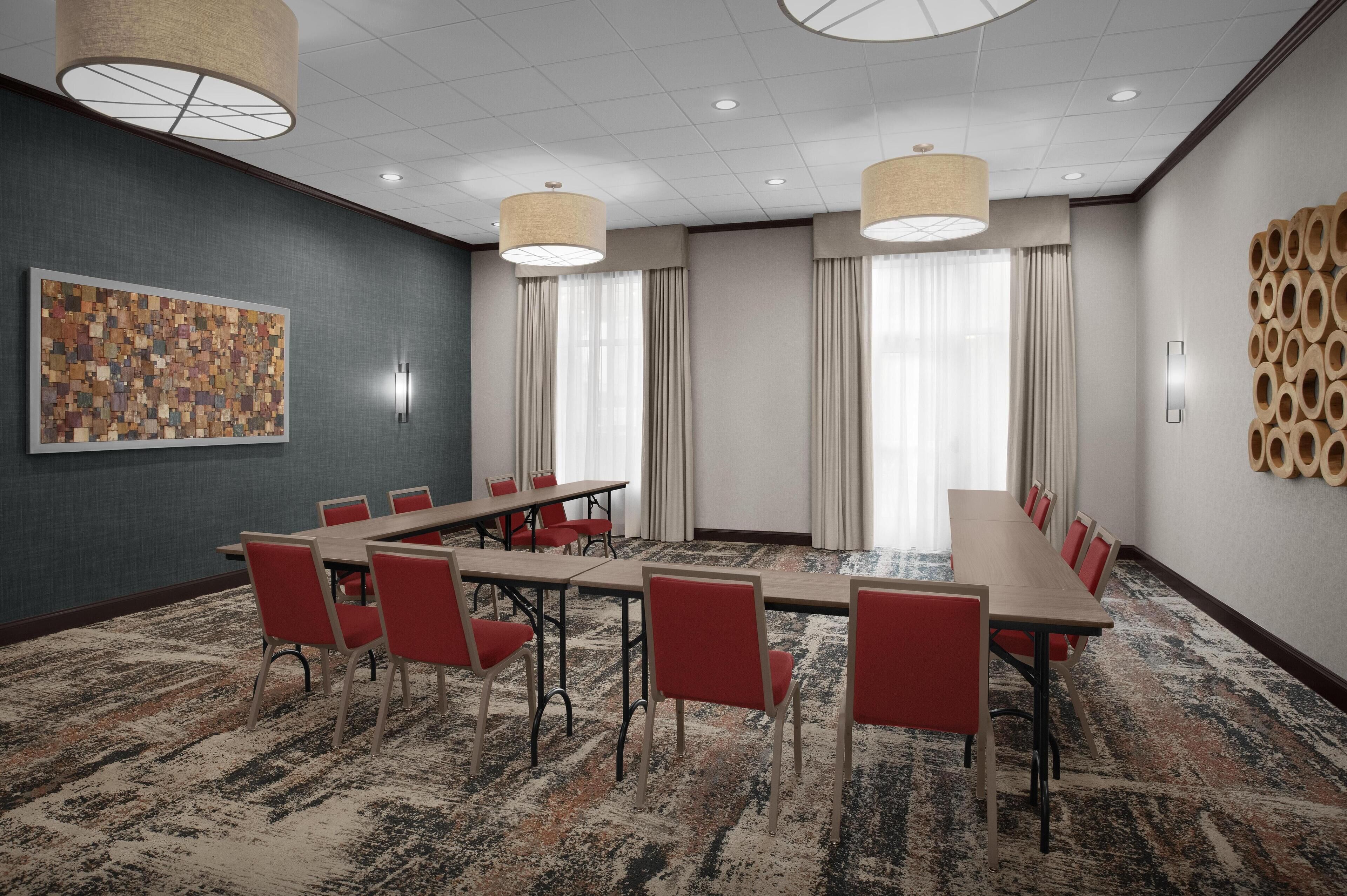 A conference room with a long table, red chairs, and a patterned carpet.