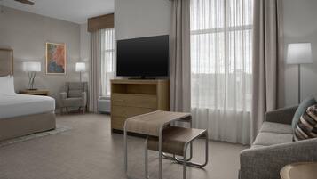 Hotelkamer met een bed, televisie, bureau, stoel, bank en raam met gordijnen.