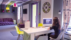 A modern office space with a white desk, yellow and white chairs, a purple sofa, and a large clock on the wall. - Good Night Hotel (Odesa)