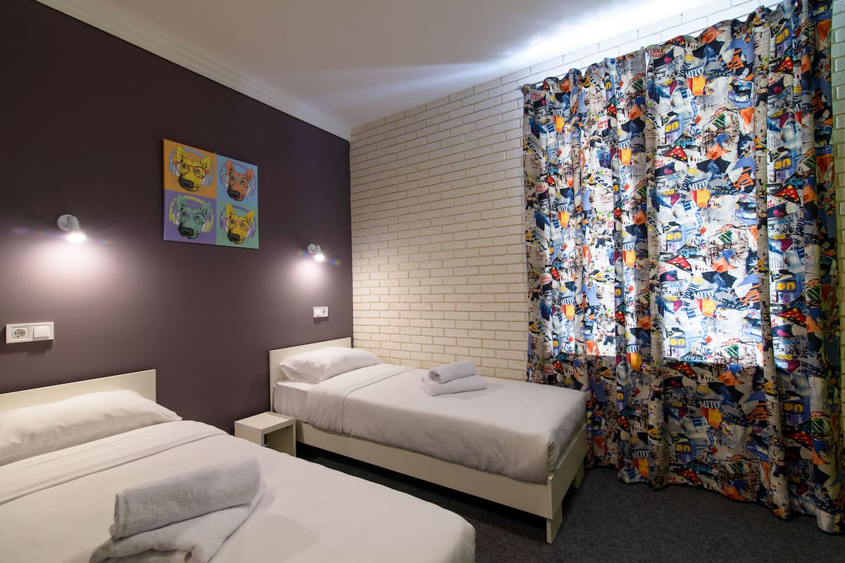 Habitación de hotel con dos camas, una pared de ladrillo y una cortina colorida.