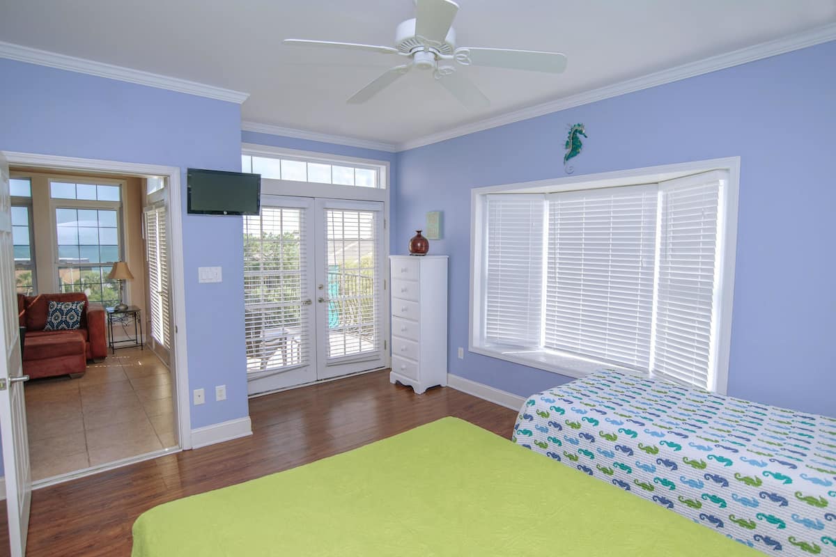 Un dormitorio con cama, cómoda, televisor y ventana con persianas.