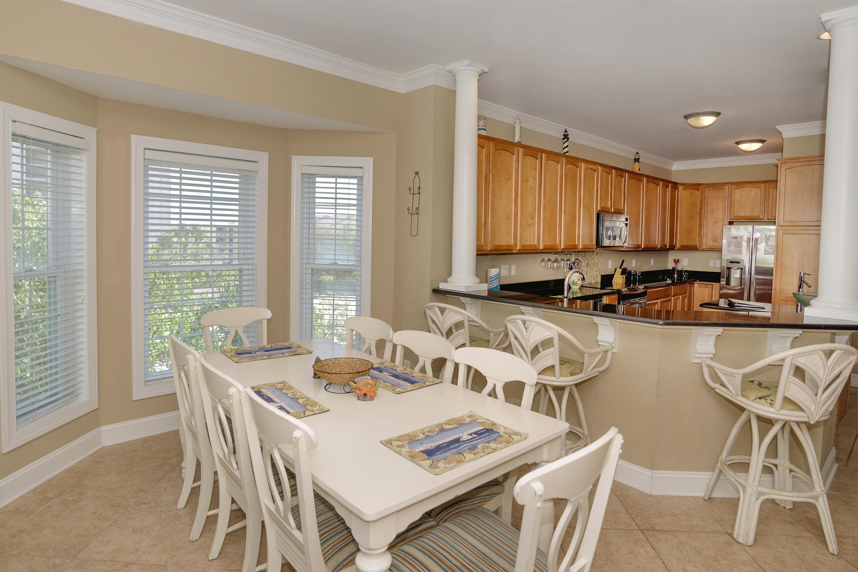 A spacious kitchen with wooden cabinets, a central island, and a dining area with white chairs and a table.