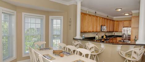 A spacious kitchen with wooden cabinets, a central island, and a dining area with white chairs and a table.