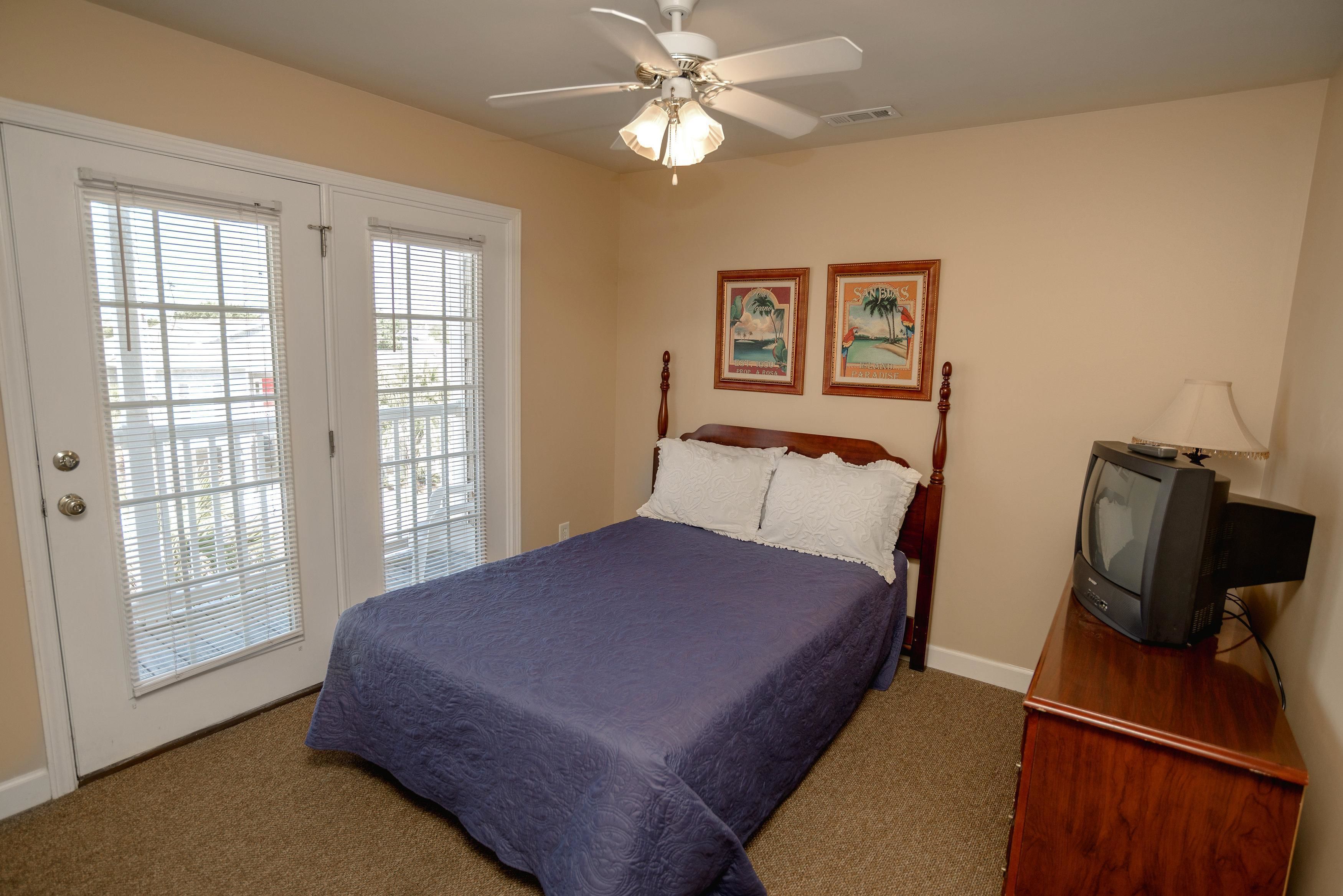 A bedroom with a bed, a ceiling fan, a television on a wooden stand, and two framed pictures on the wall.