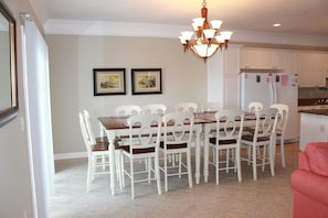A dining area with a wooden table and white chairs, a chandelier, and a refrigerator with magnets.