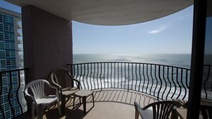 A balcony with a view of the ocean, featuring two white plastic chairs and a wooden chair. - The Palms 1701 Villa 4 bedroom By Affordable Large Properties (Myrtle Beach)