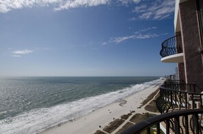Blick auf einen Strand von einem Balkon mit Geländer, Meer und Badegäste.
