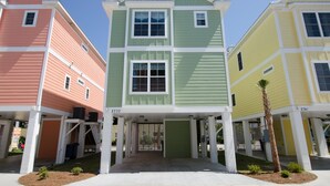 A row of colorful townhouses with a central green house, each with a garage and a small front yard. - South Beach Cottages 4 bedroom By Affordable Large Properties (Myrtle Beach)