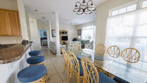 A dining area with a glass table and wicker chairs, a kitchen with wooden cabinets, and a living area with a sofa and television.