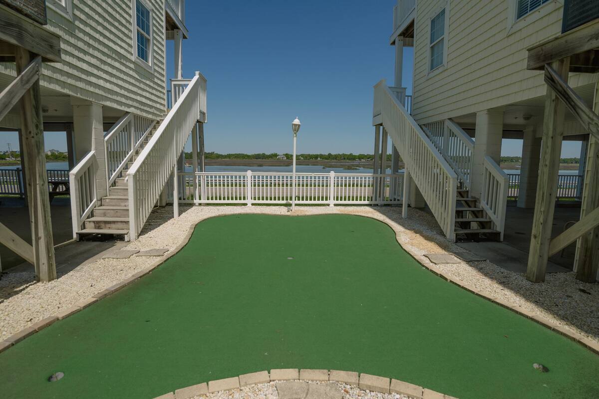 Un parcours de mini-golf doté d’un tapis vert pour les putts, entouré de structures en bois avec des garde-corps et une clôture blanche.