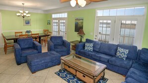 A living room with blue sofas, a glass coffee table, and a ceiling fan.