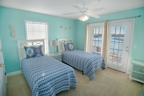 Quarto com duas camas, um ventilador de teto e vista para o exterior através de uma porta.
