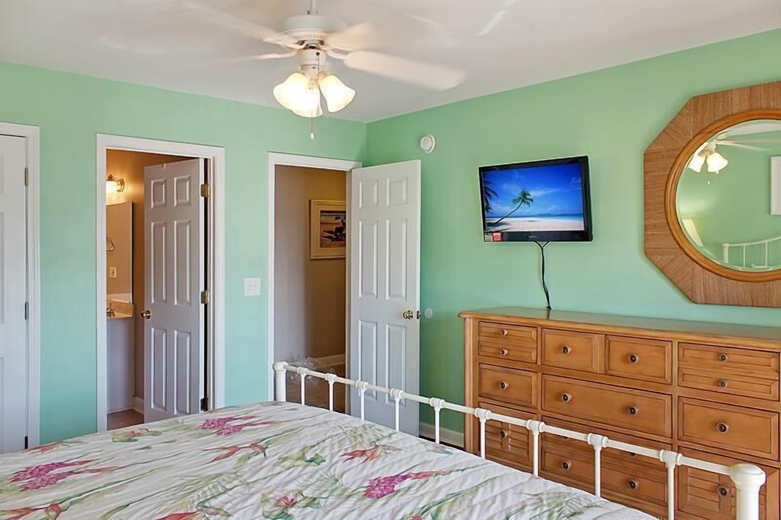 A bedroom with a bed, a dresser, a television, and a ceiling fan.