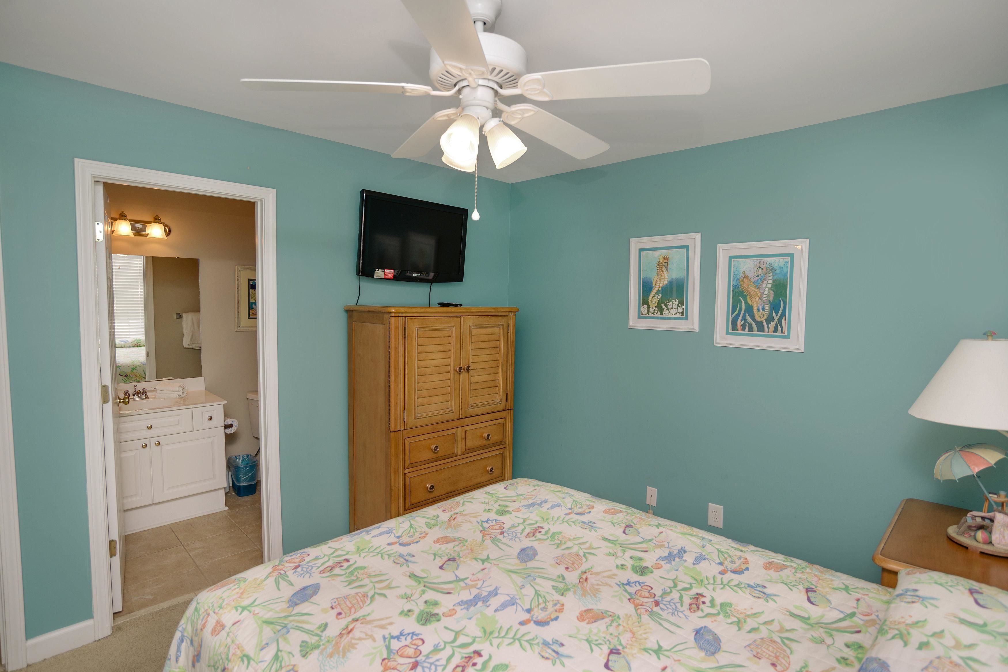 A bedroom with a bed, a ceiling fan, a TV, a wooden cabinet, and two framed pictures on the wall.