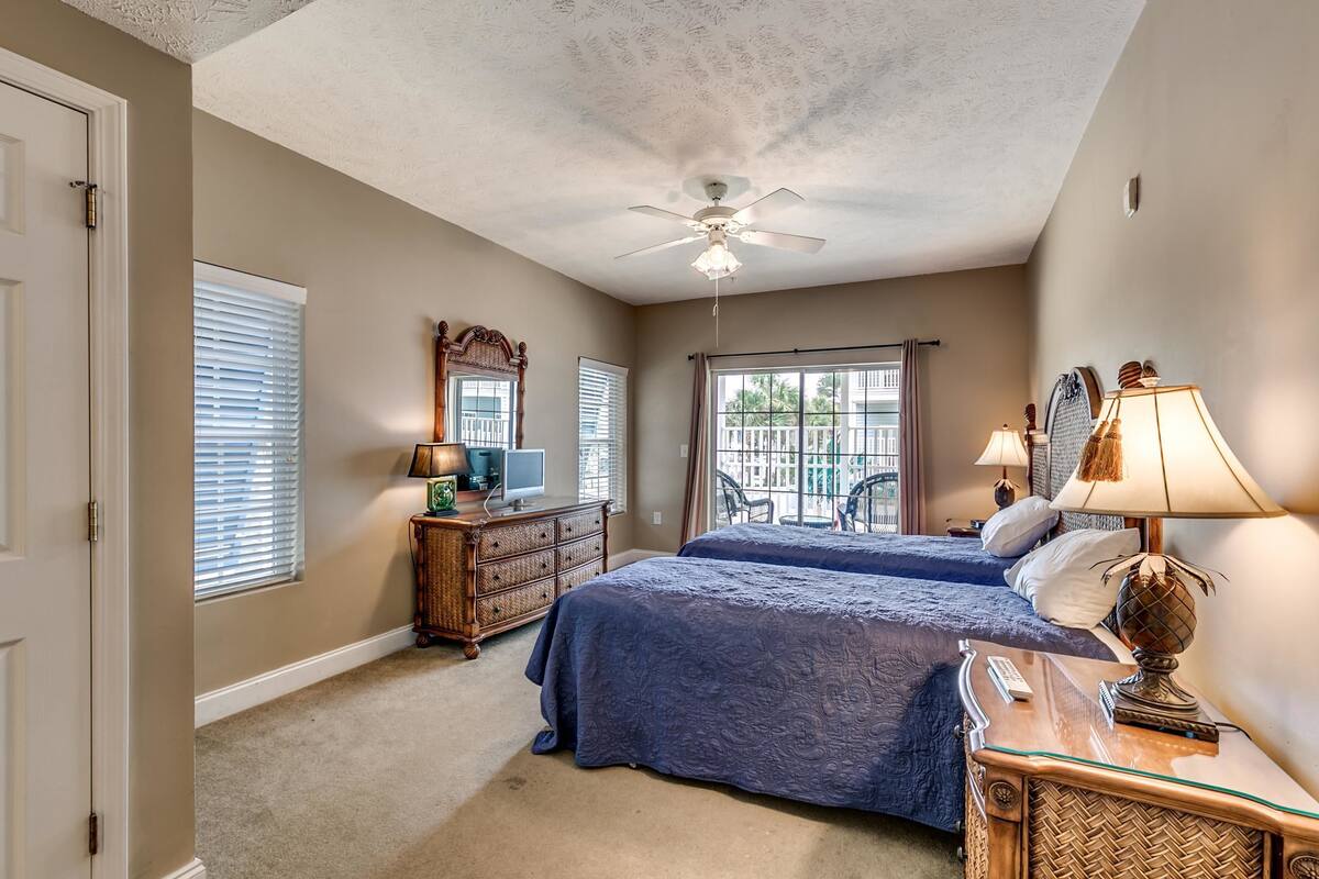 A bedroom with two beds, a ceiling fan, a dresser, and a window with blinds.