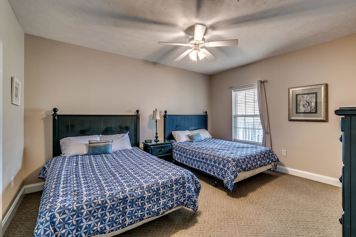 A bedroom with two beds, a ceiling fan, and a window with curtains.