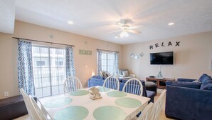 A living room with a dining area, a ceiling fan, a TV mounted on the wall, and a 'RELAX' sign. - Myrtle Beach 101A Villa 4 bedroom By Affordable Large Properties (Myrtle Beach)