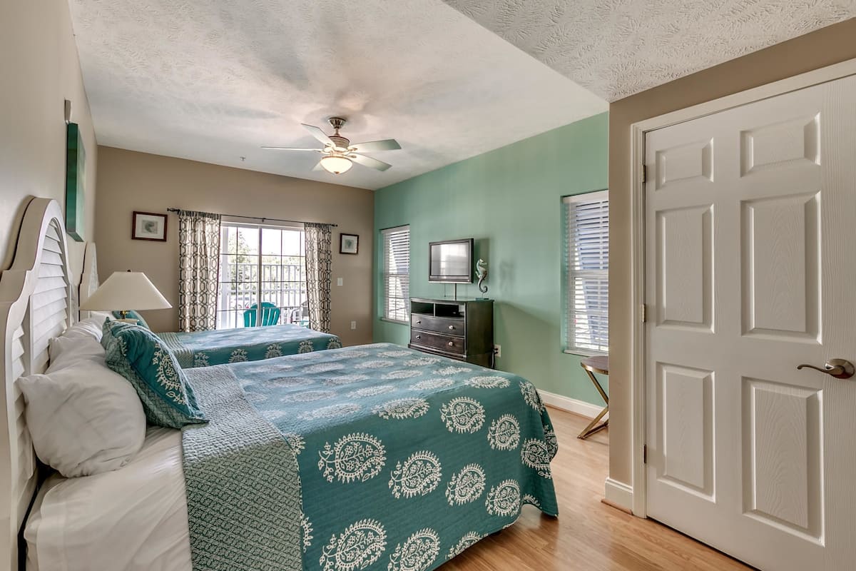 A bedroom with two beds, a ceiling fan, a TV, and a door.