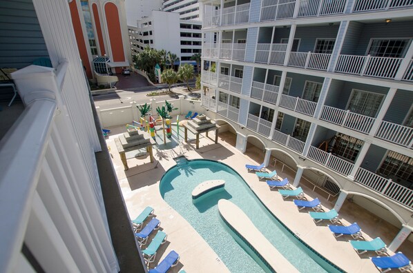 Zona de piscina con sillones de descanso y una piscina pequeña, rodeada por un edificio de varios pisos con balcones.