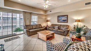 A spacious living room with a large window, a ceiling fan, a sofa set, a coffee table, and a floor lamp. - Myrtle Beach 101A Villa 4 bedroom By Affordable Large Properties (Myrtle Beach)