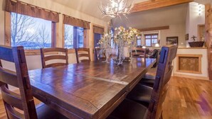 Un espace repas comprenant une table en bois, des chaises, un lustre et une vue sur l’extérieur.